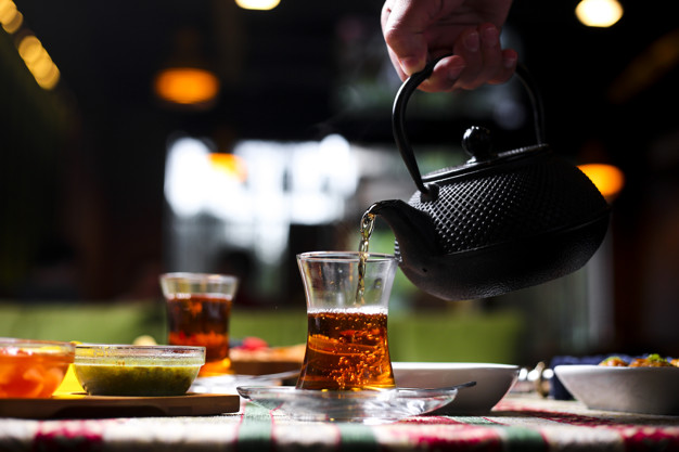 man pouring tea into armudu glass from stone teapot horizontal